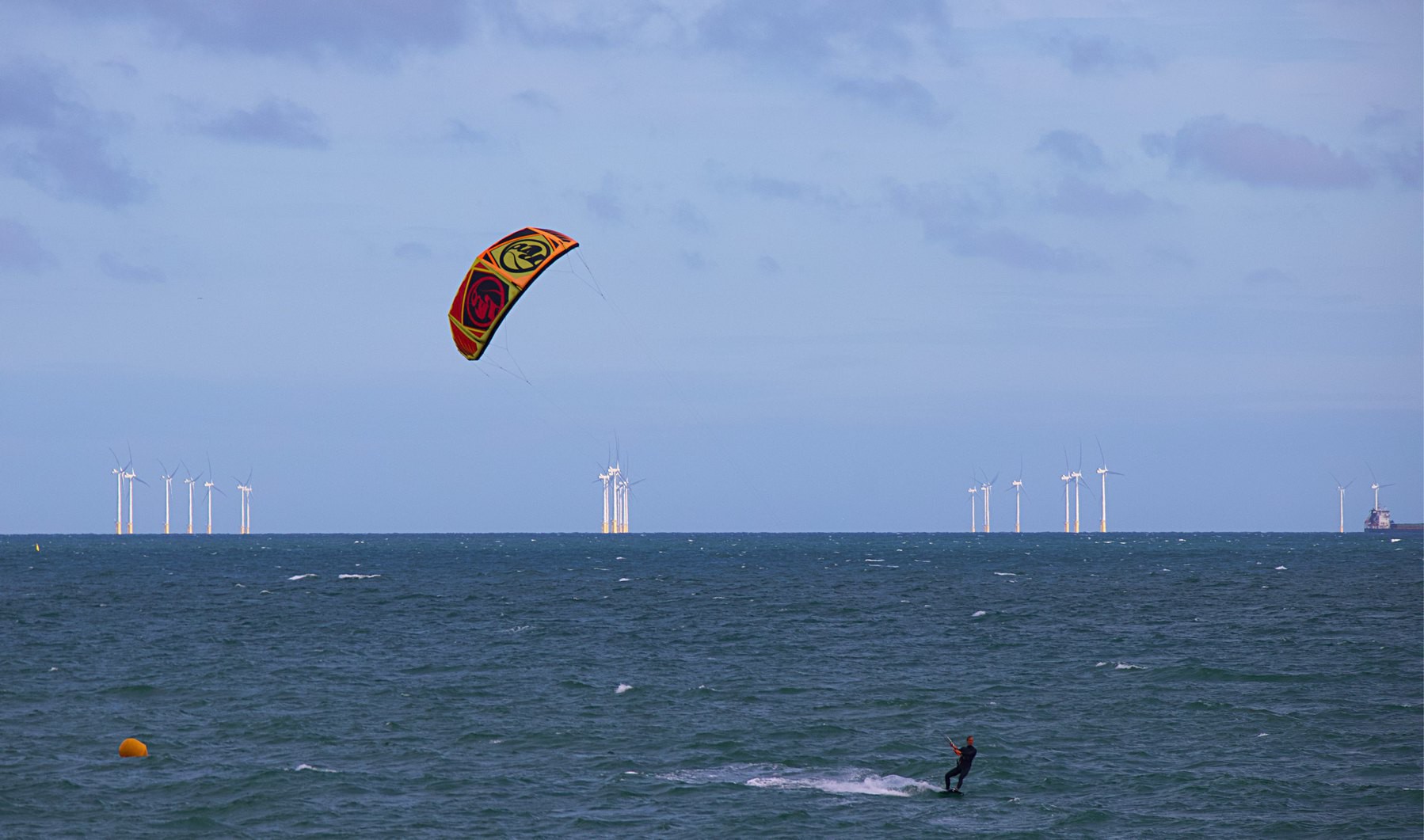 A kitesurfer surfing in front of the Rampion Wind Farm. 