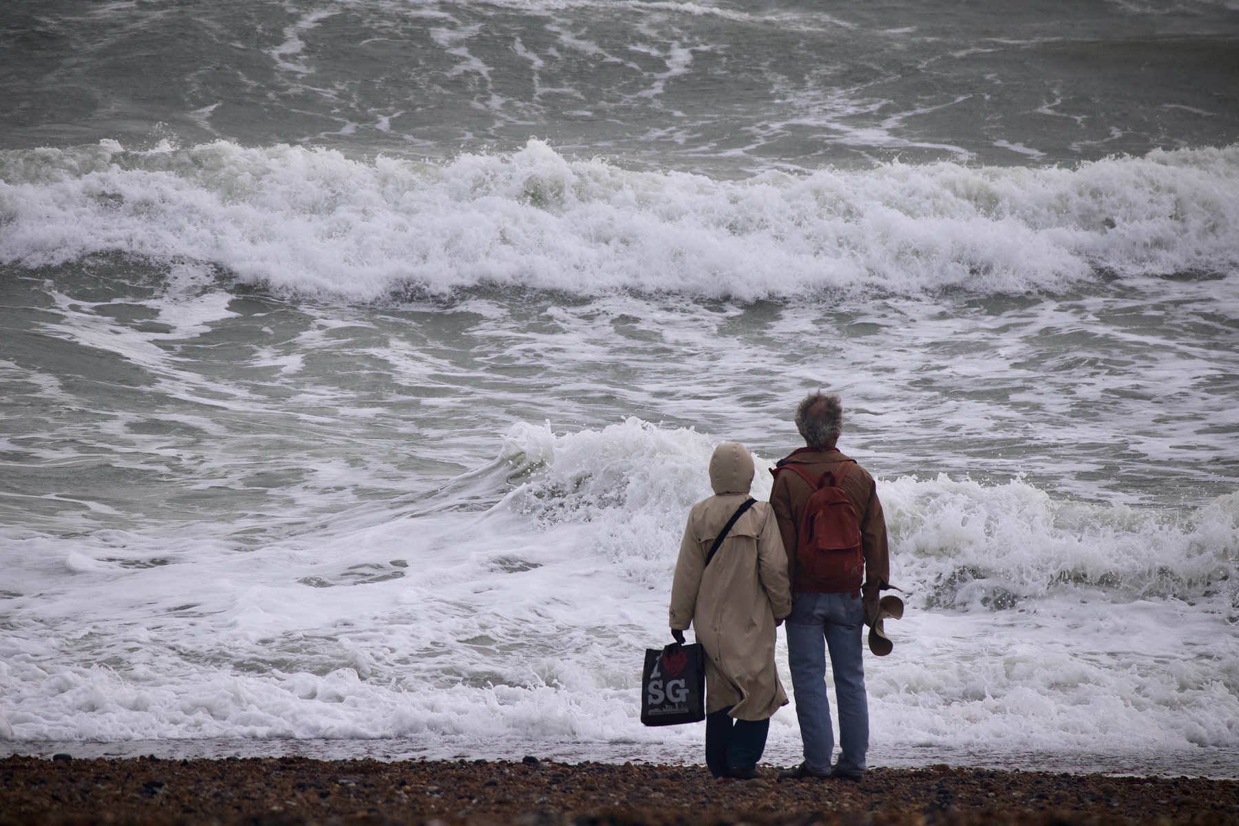 A couple stands on Shoreham Beach facing the waves. 