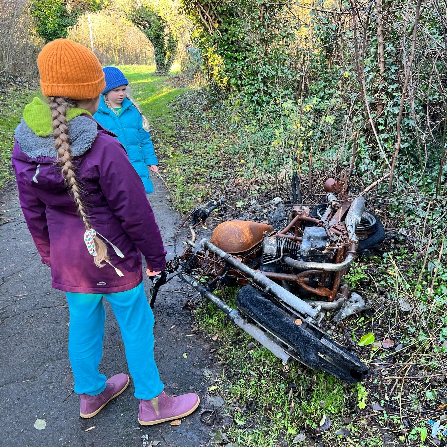 Two girls looking at a burnt-out motorcycle on a path in Knowle West.