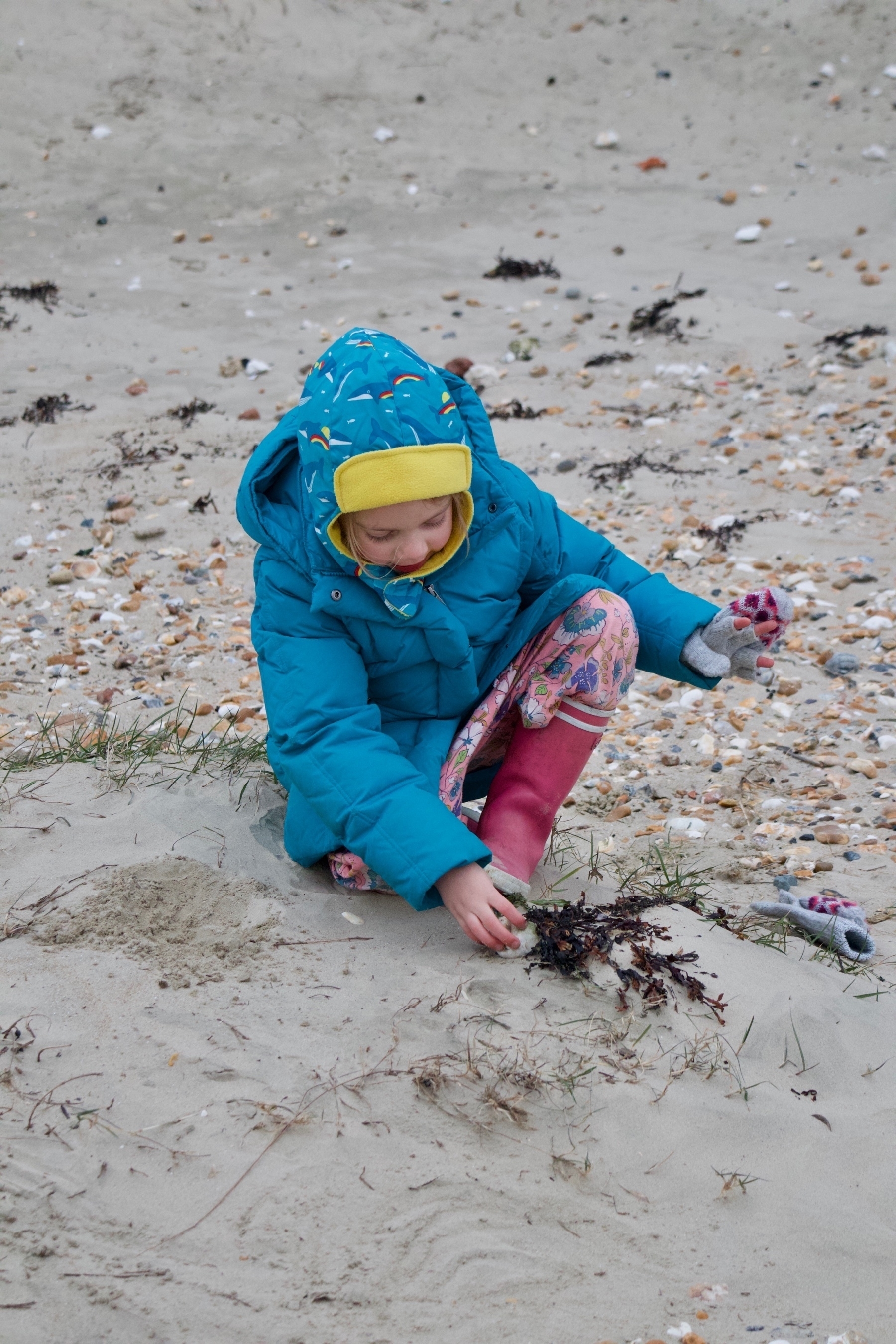 A girl, wrapped up for winter weather, playing on a beach. 