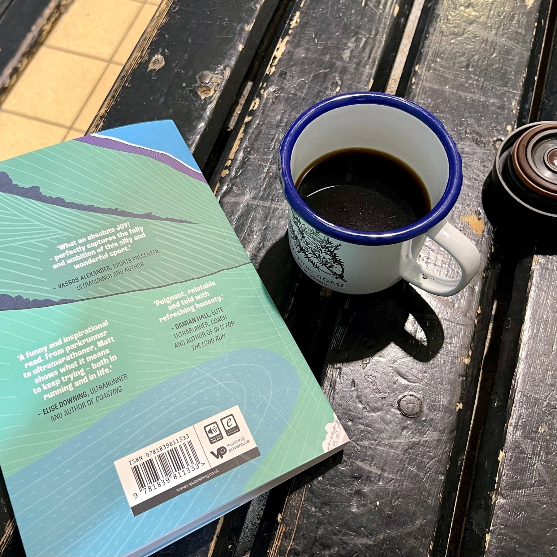 A book and an enamal mug of coffee by a swimming pool. 