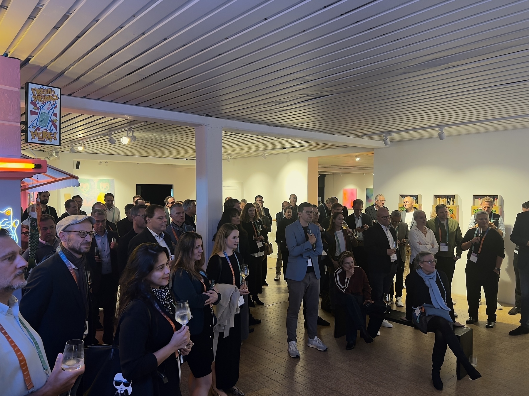 A group of people is attentively gathered at an indoor event or gallery.