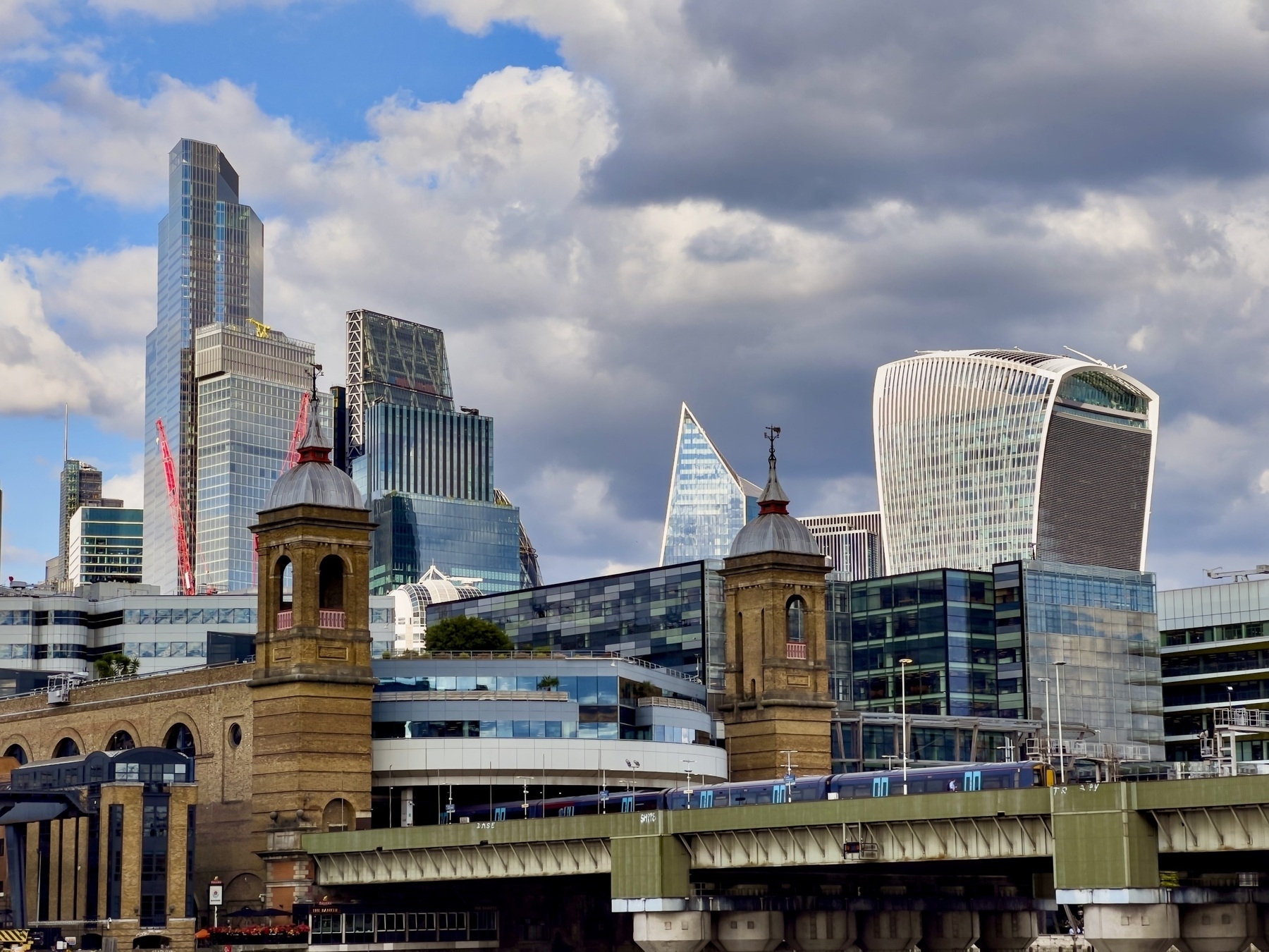 A London cityscape features modern skyscrapers mixed with historic architecture under a partly cloudy sky.