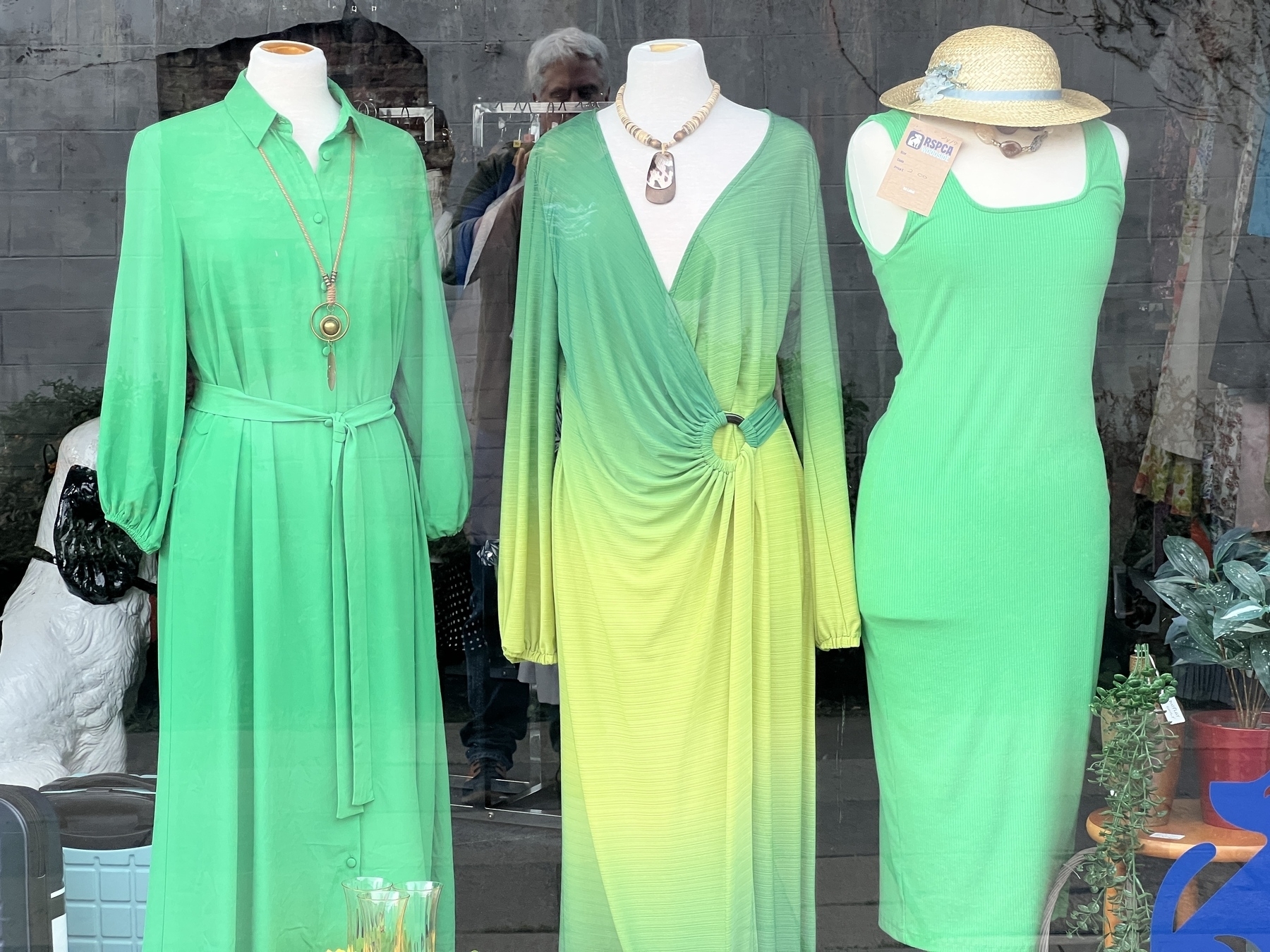 Three mannequins display green dresses and garments, with a variety of styles including long-sleeved, wrap, and sleeveless, accompanied by a hat.