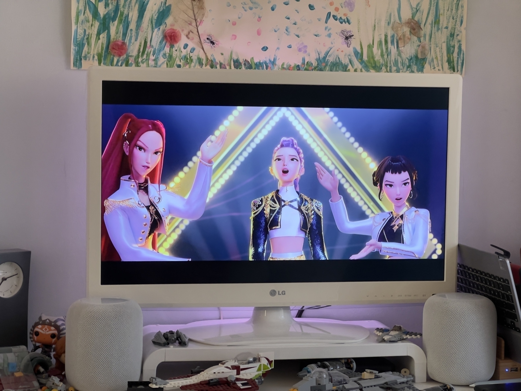 Three animated characters are performing energetically on a screen with colorful lights in the background.