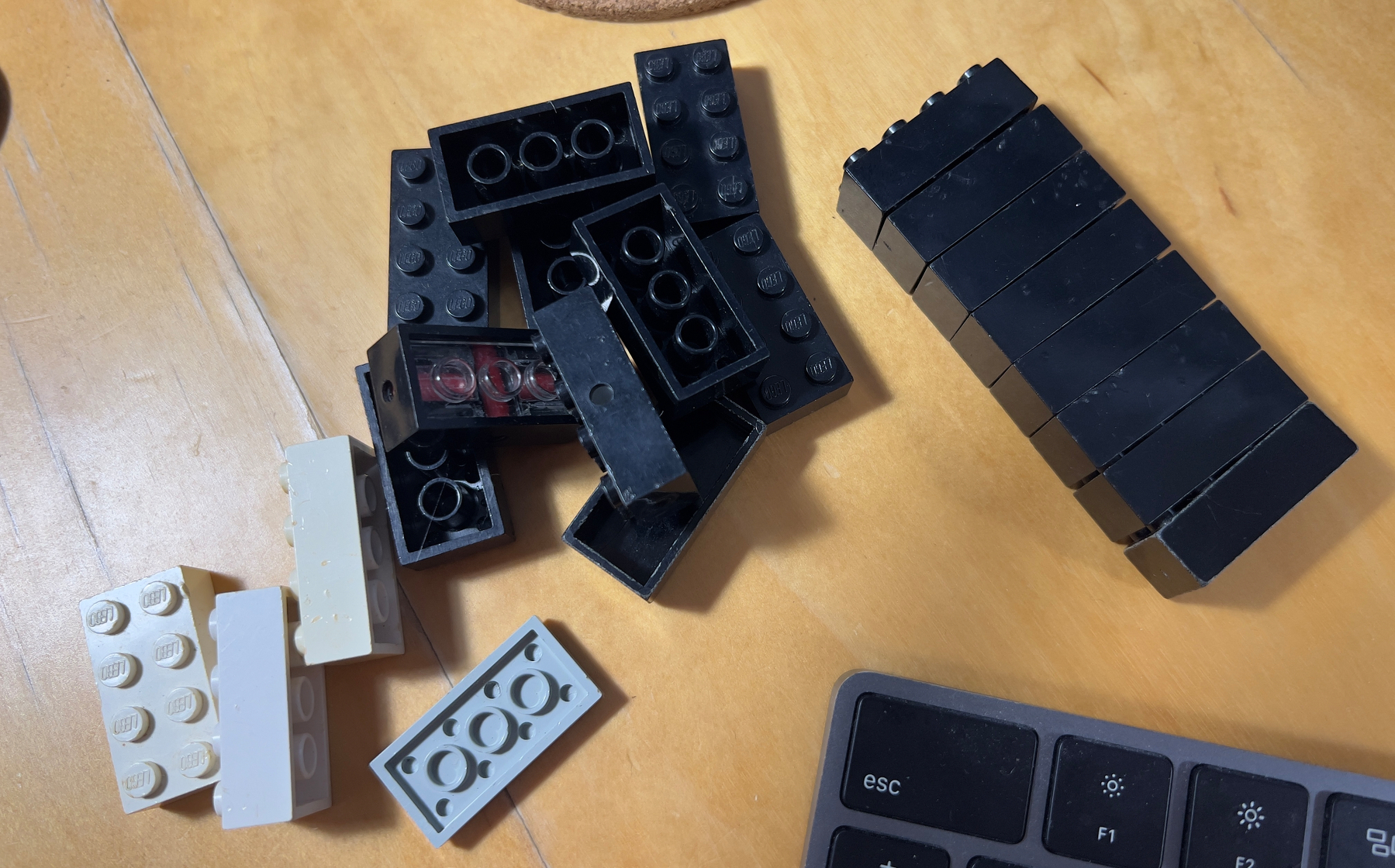 A collection of black and white LEGO bricks is scattered on a wooden surface next to a computer keyboard.