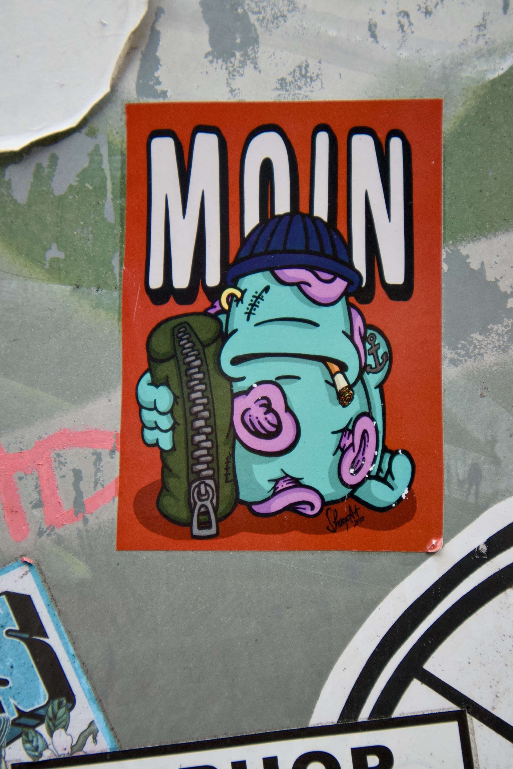 A colorful sticker features a cartoonish blue creature with a beanie, holding a bottle, and the text "MOIN" above it.