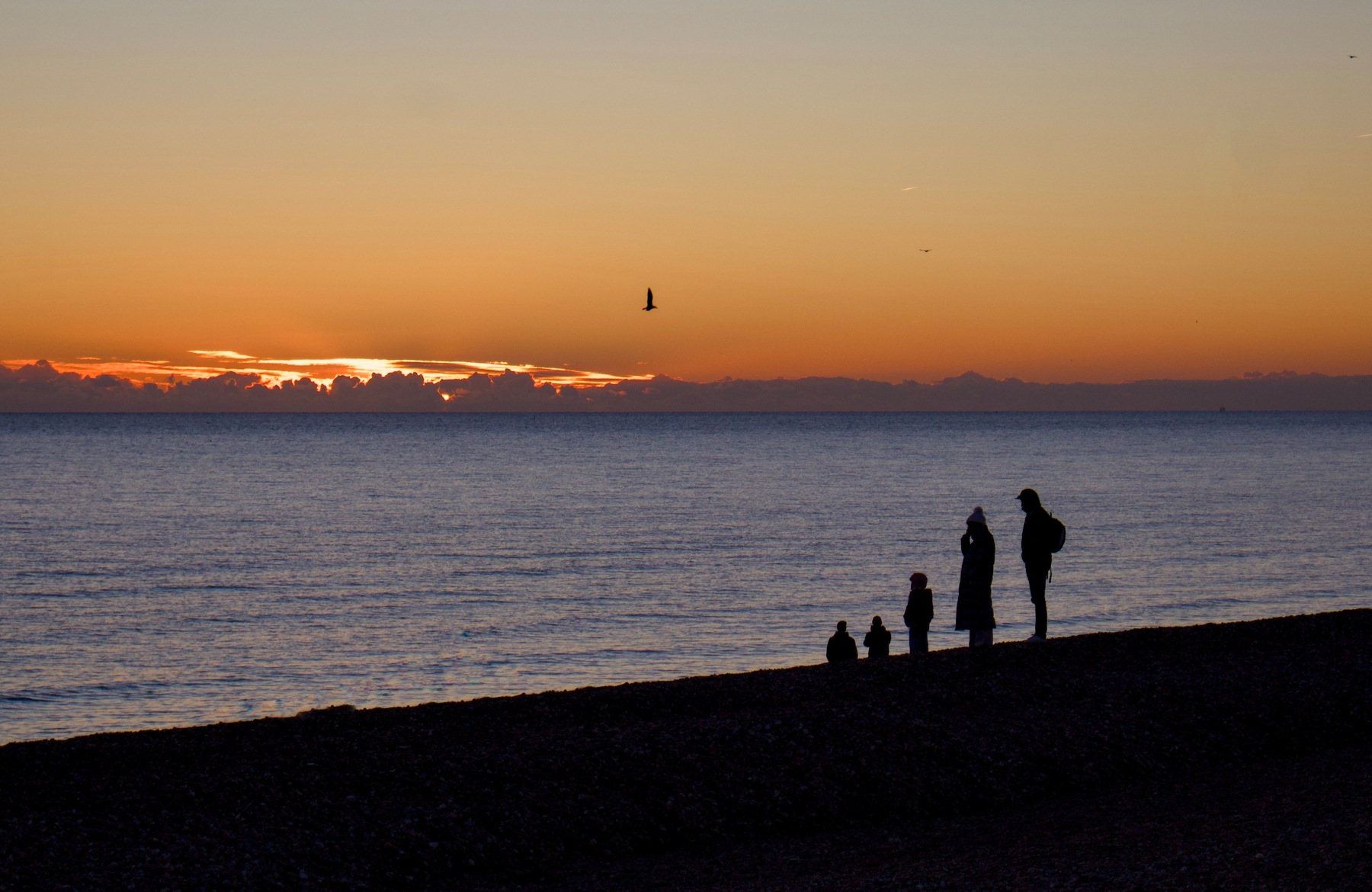 A family stands on the beach at sunset, silhouetted against the horizon.