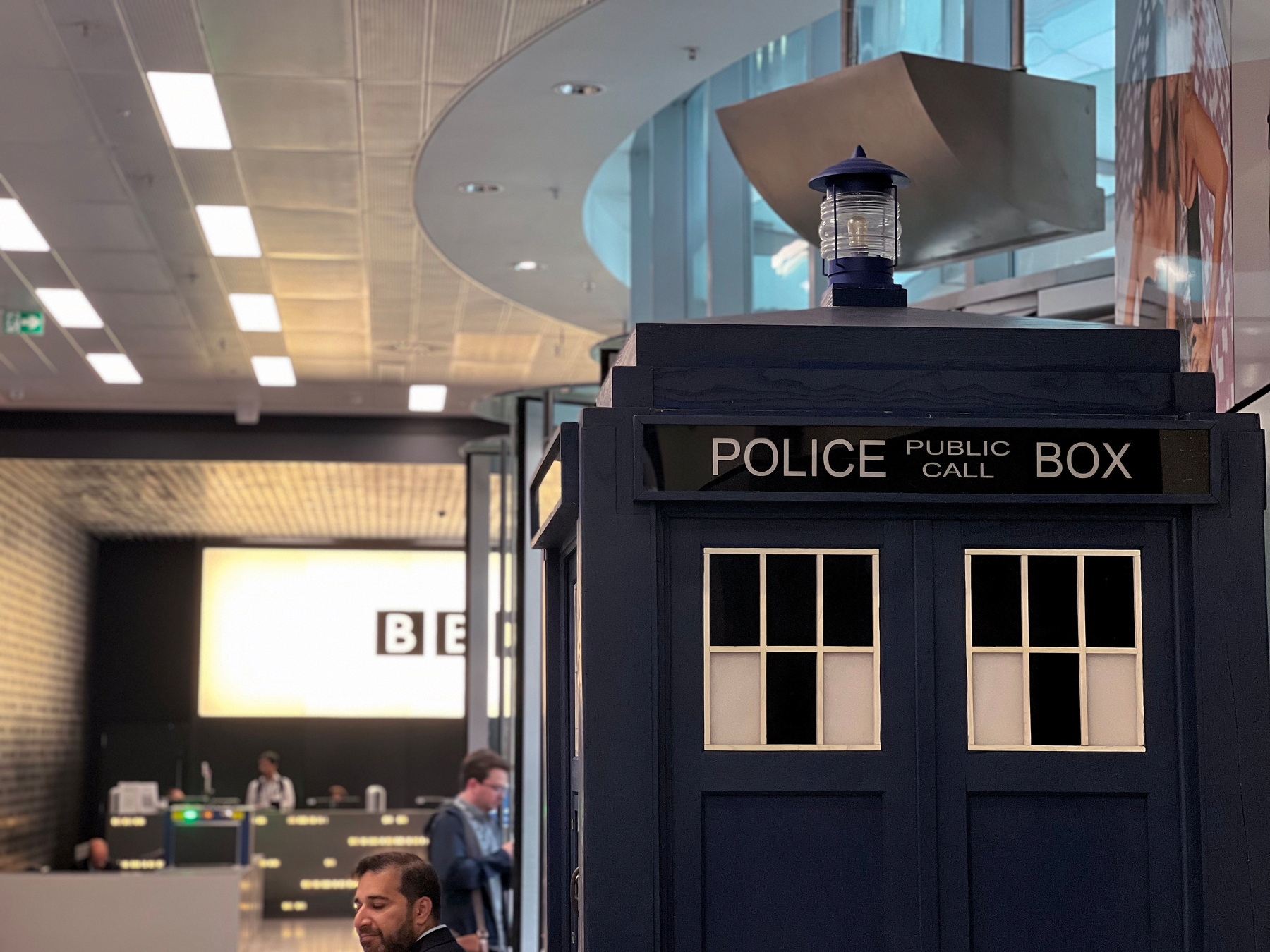 A man is standing near a blue police box in a modern indoor setting.