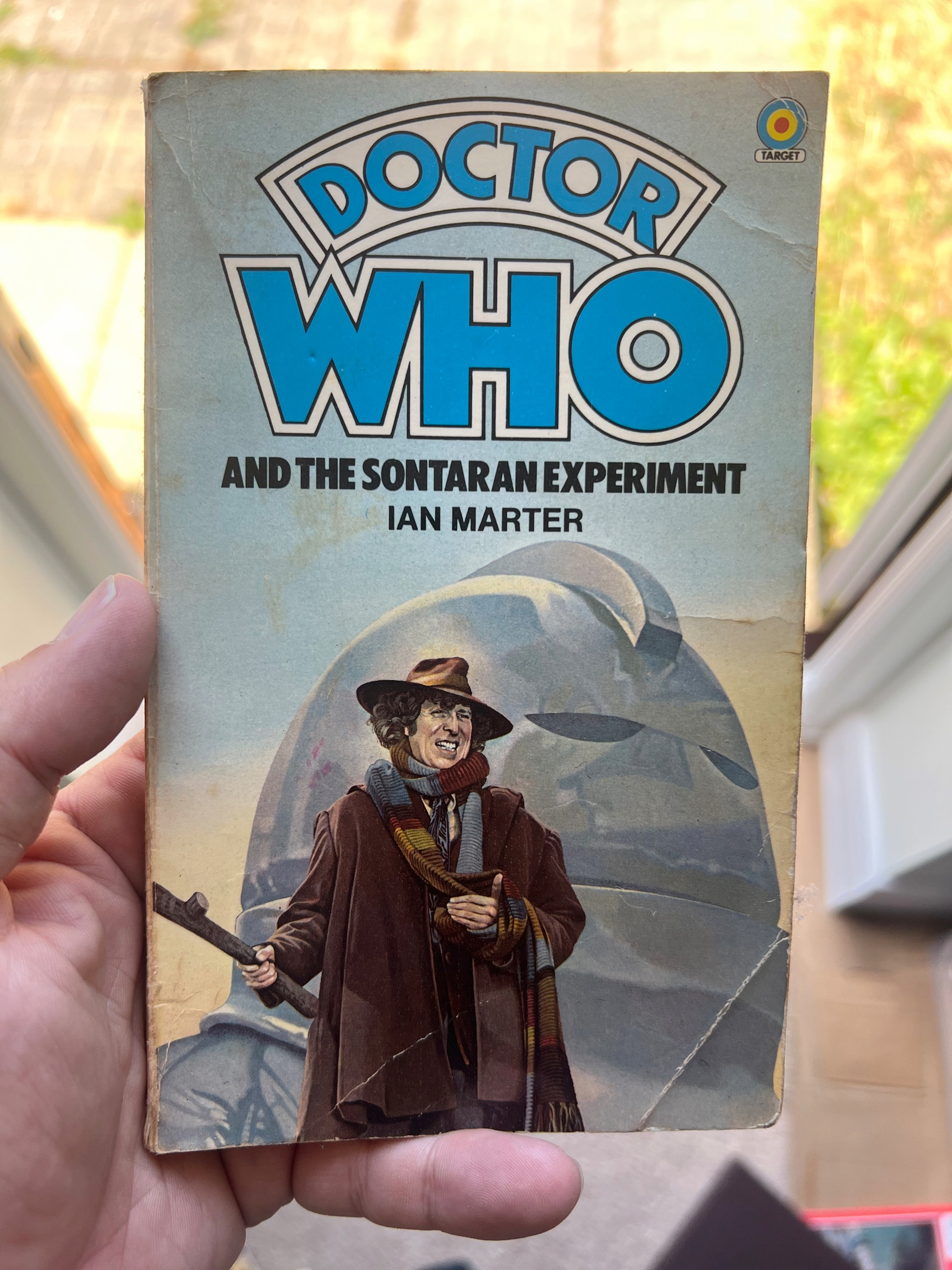 A person is holding a paperback copy of the book Doctor Who and the Sontaran Experiment by Ian Marter, featuring a cover illustration of the Fourth Doctor and a Sontaran.