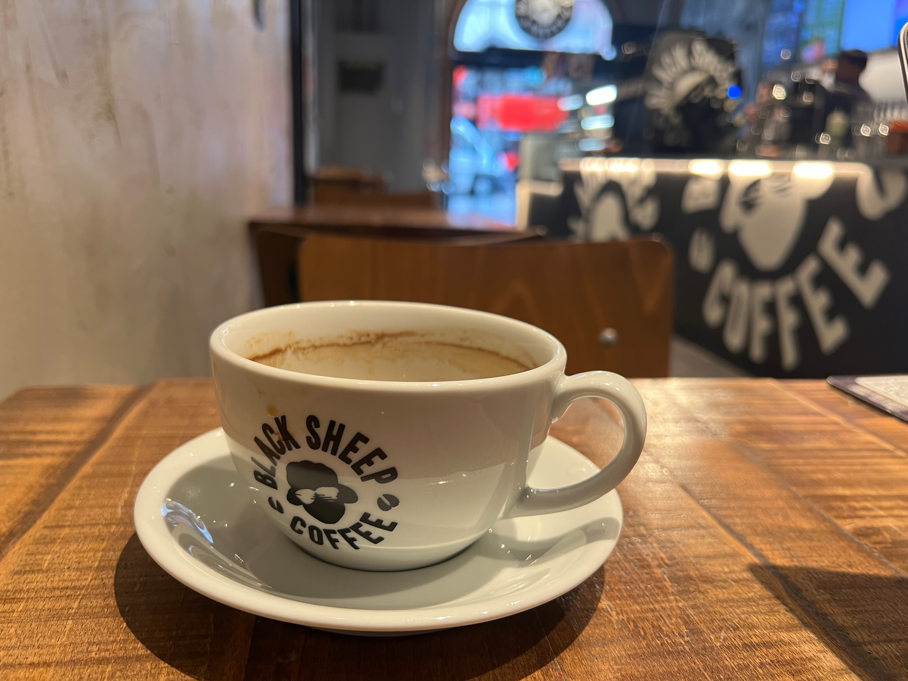 A long black in a cup labeled Black Sheep Coffee sits on a wooden table in a café.