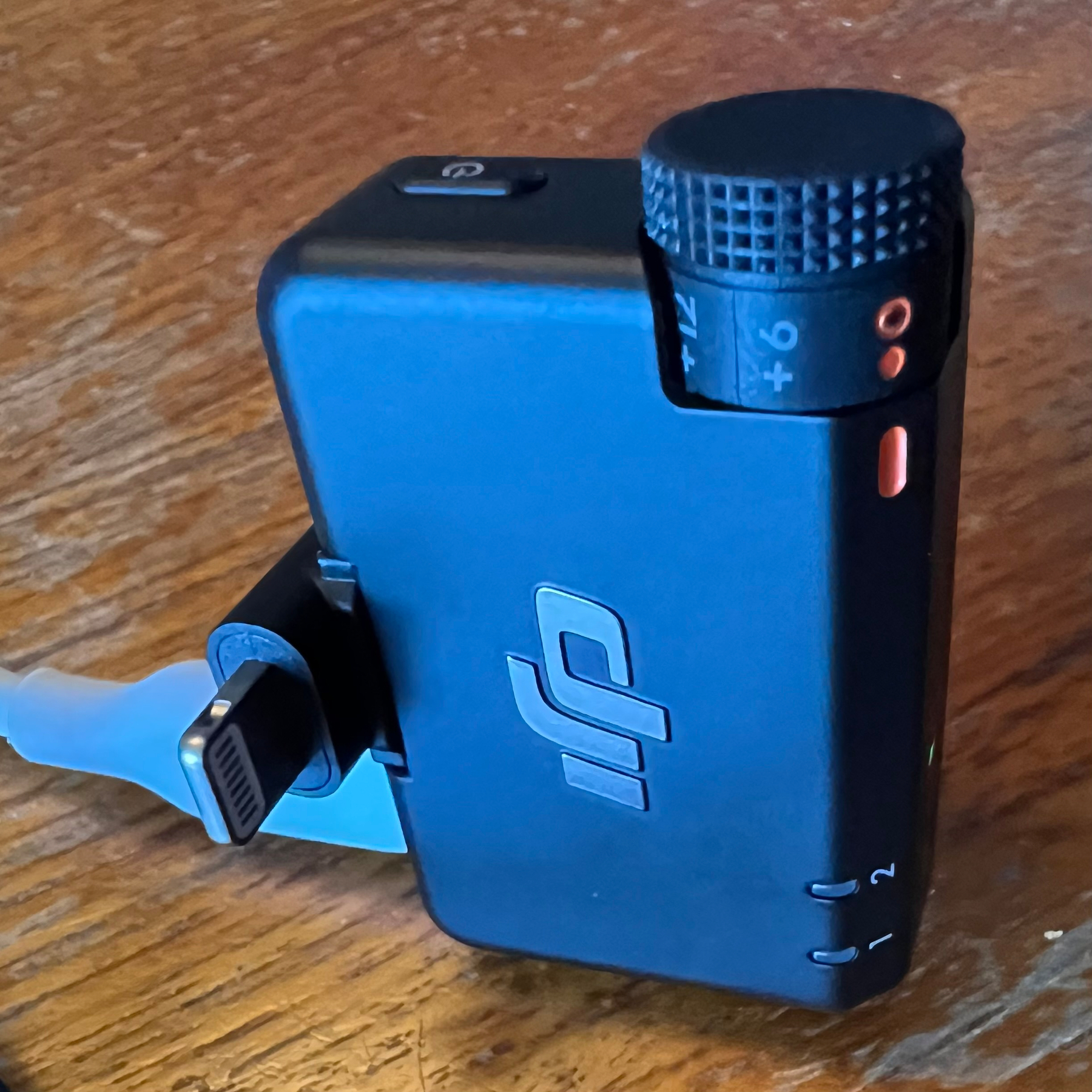 A DJI wireless microphone system with an attached Lightning connector is placed on a wooden surface.