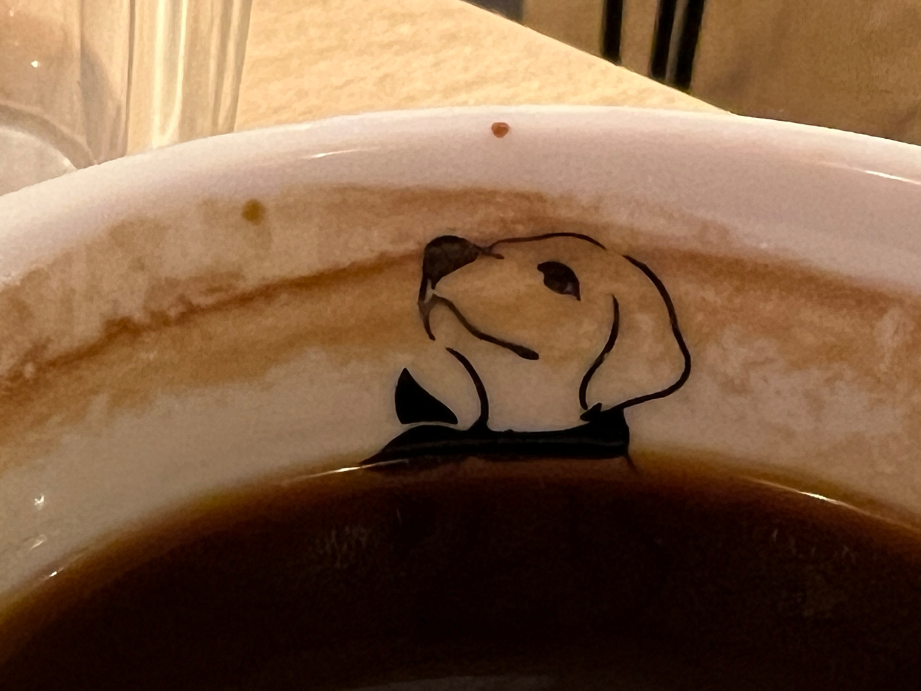 A cup of coffee with a design near the rim resembling a dog's face.