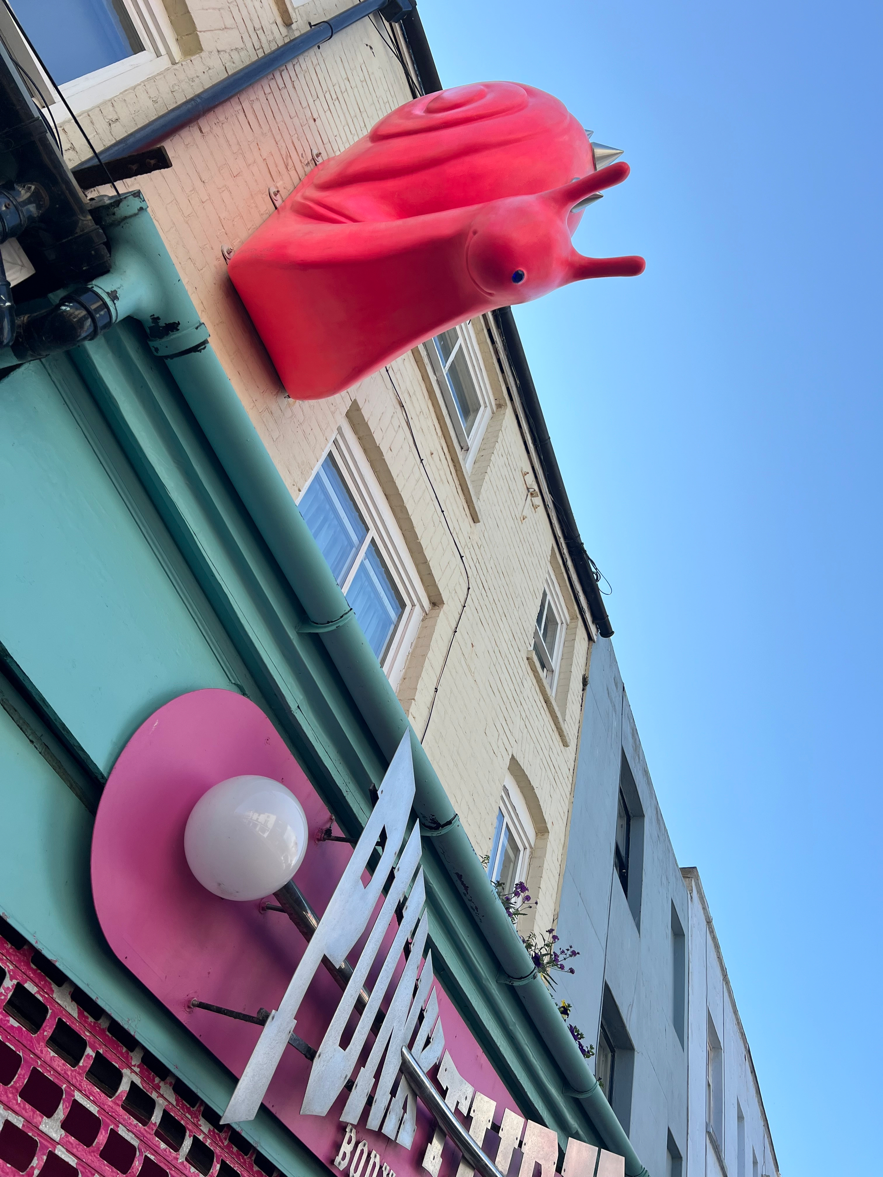 A large red snail sculpture is mounted on the exterior wall of a building with a clear blue sky in the background.