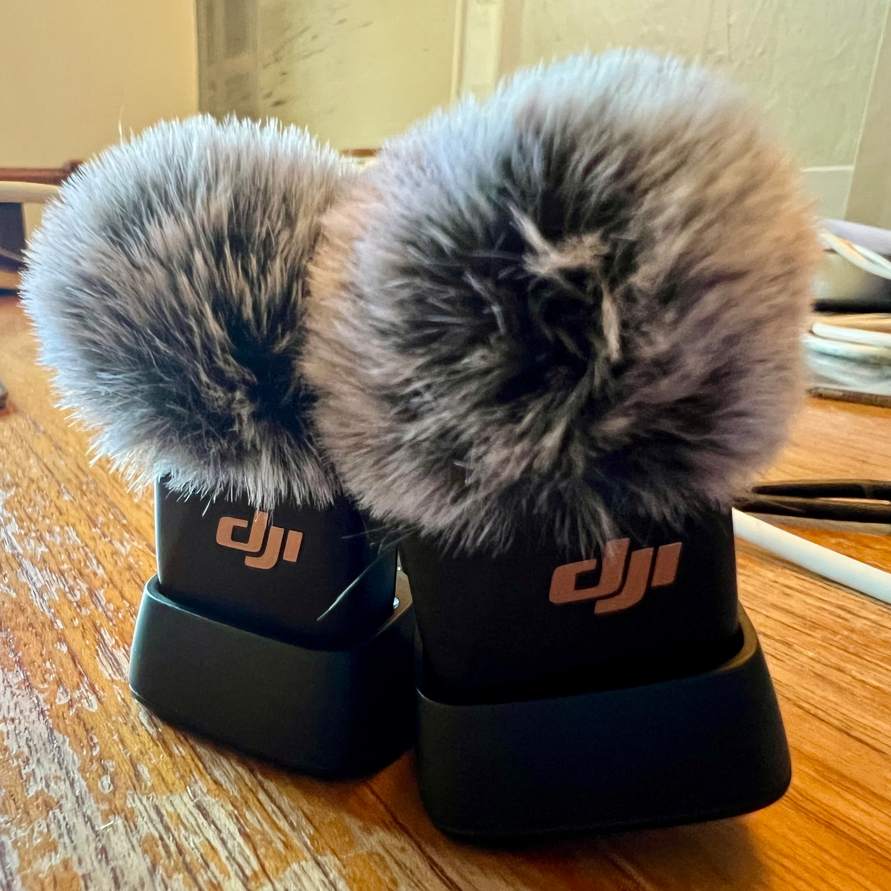Two DJI microphones with furry windshields are placed on a wooden surface, one in front of the other.